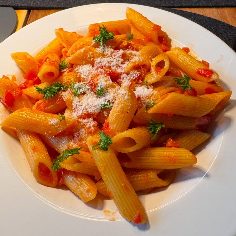 Penne in roter Tomatensauce mit Parmesan und Petersilie auf einem weißen Teller