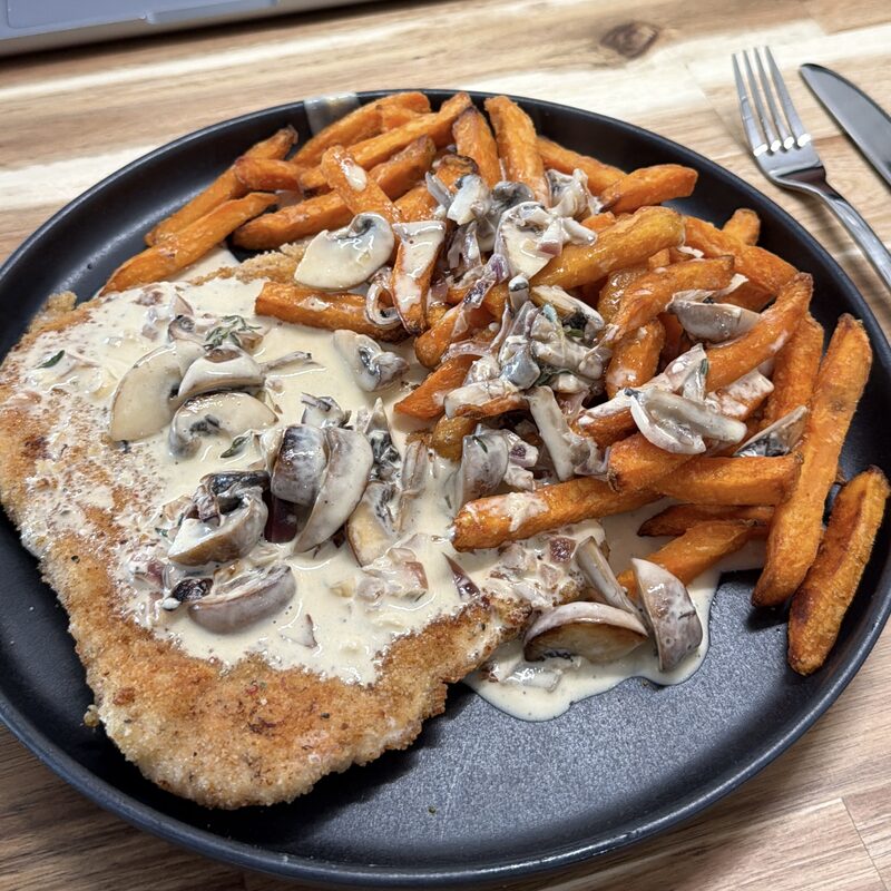 Paniertes Schnitzel mit Champignonrahmsoße und Pommes auf einem dunklen Teller