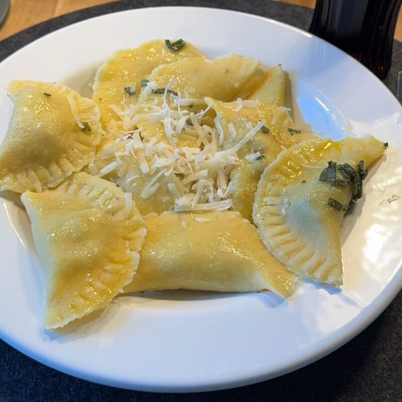 Selbstgemachte Ravioli mit Salbeibutter und geriebenem Käse auf einem weißen Teller